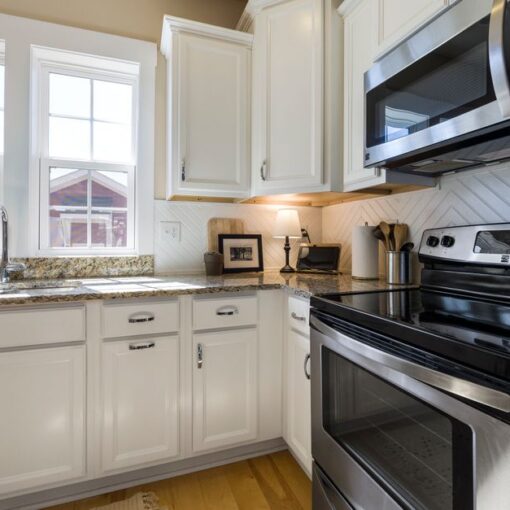 Bright white kitchen with granite counters, double sink under two windows, and stainless steel range and microwave beside a backsplash.