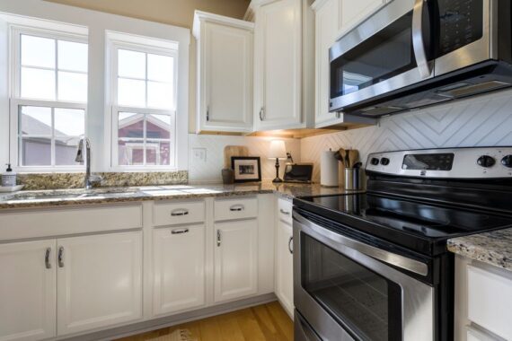 Bright white kitchen with granite counters, stainless steel stove and microwave, and large front windows.