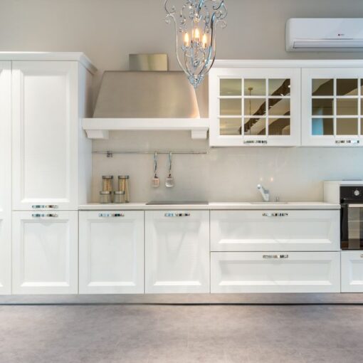 White modern kitchen with tall cabinet, stainless range hood, glass-front upper cabinets, built-in oven, and a chandelier above."related to kitchen design"