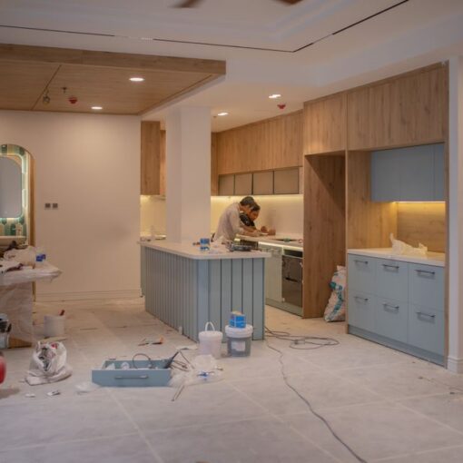 Kitchen under renovation with a blue island, wooden cabinets, and a worker at the countertop.
