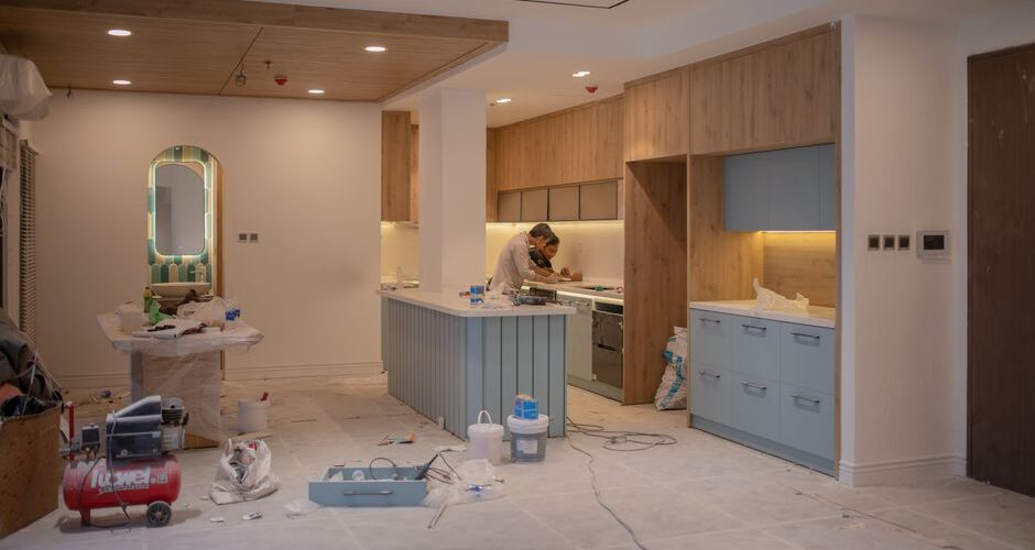 Kitchen under renovation with a blue island, wooden cabinets, and a worker at the countertop.