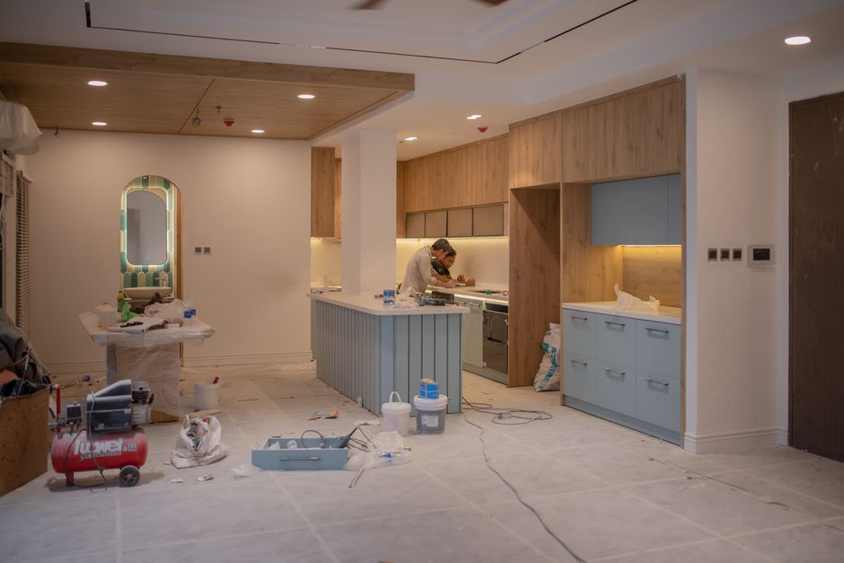 Kitchen under renovation with a blue island, wooden cabinets, and a worker at the countertop.
